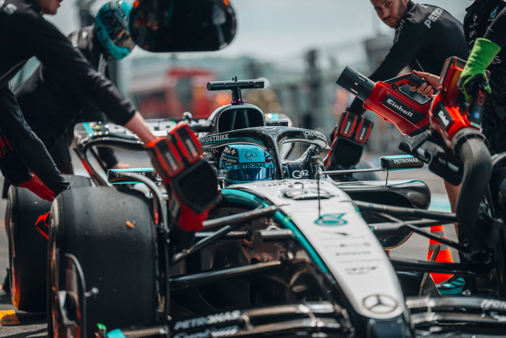 Ein Mercedes-AMG PETRONAS Formel-1-Auto beim Boxenstopp. Teammitglieder nutzen Einhell Akku-Gebläse, um Fahrzeugkomponenten zu kühlen. Die Crew arbeitet konzentriert und präzise.