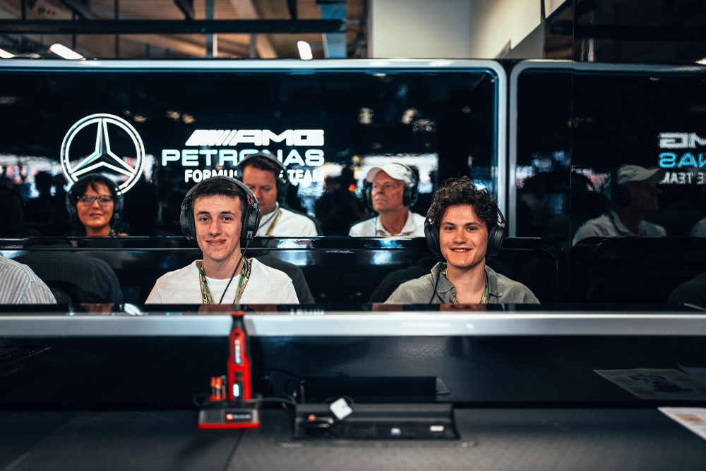 Zwei Männer sitzen in der Garage des Mercedes-AMG PETRONAS Formel-1-Teams, tragen Headsets und genießen das exklusive Erlebnis hinter den Kulissen. Im Vordergrund ist ein rotes Einhell-Gerät zu sehen.