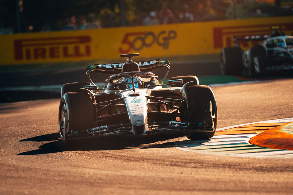 Ein Mercedes-AMG PETRONAS Formel-1-Auto fährt bei Sonnenschein auf einer Rennstrecke während eines Grand Prix. Das Fahrzeug nimmt eine Kurve mit hoher Geschwindigkeit, ein weiteres Auto ist im Hintergrund zu sehen.