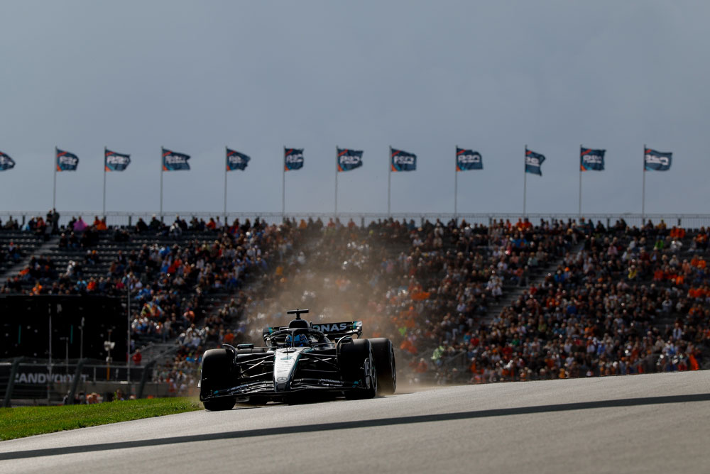 Ein Mercedes-AMG PETRONAS Formel-1-Auto fährt während eines Rennens an voll besetzten Tribünen vorbei. Im Hintergrund wehen zahlreiche Fahnen, was für eine mitreißende Atmosphäre sorgt.