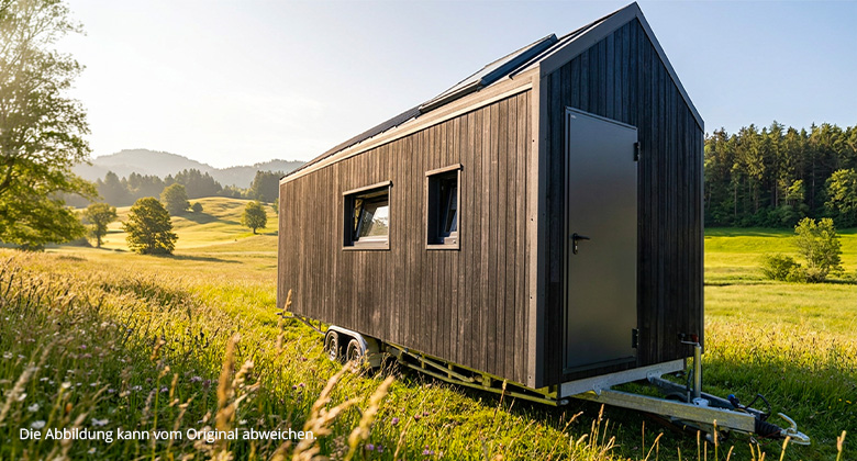 Außenansicht eines modernen Tiny Houses mit dunkler Holzfassade auf einem Anhänger in einer grünen Hügellandschaft.