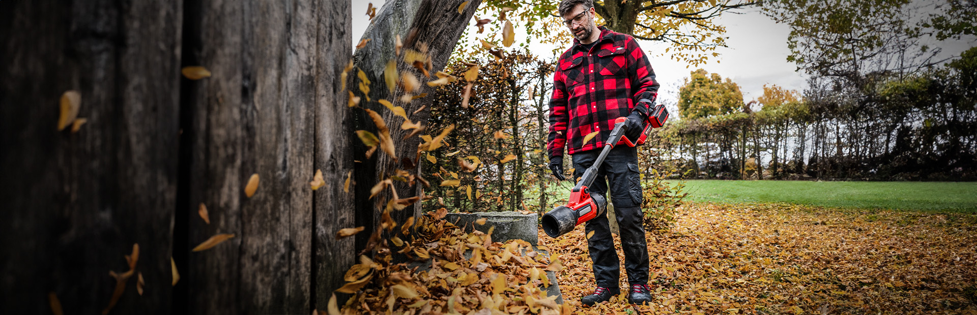 Ein Mann bläst mit einem Einhell Akku-Laubbläser Herbstlaub vor einem Baumstamm weg.