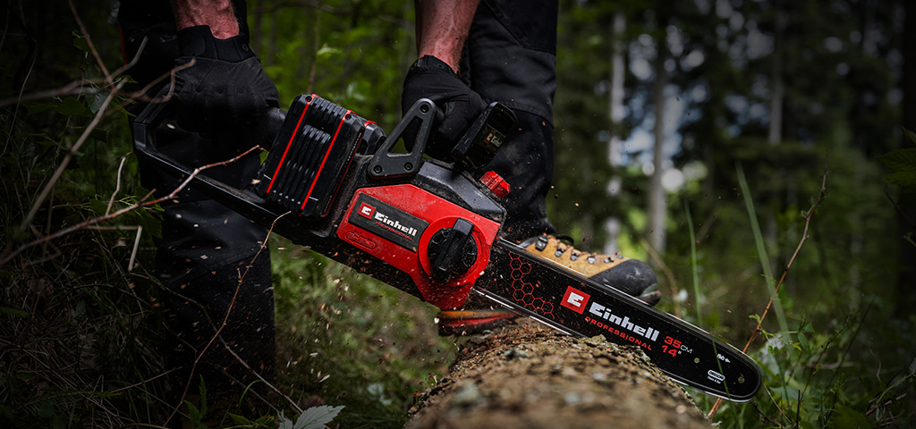 Ein Mann sägt mit einer Einhell Akku-Kettensäge einen Baumstamm im Wald.