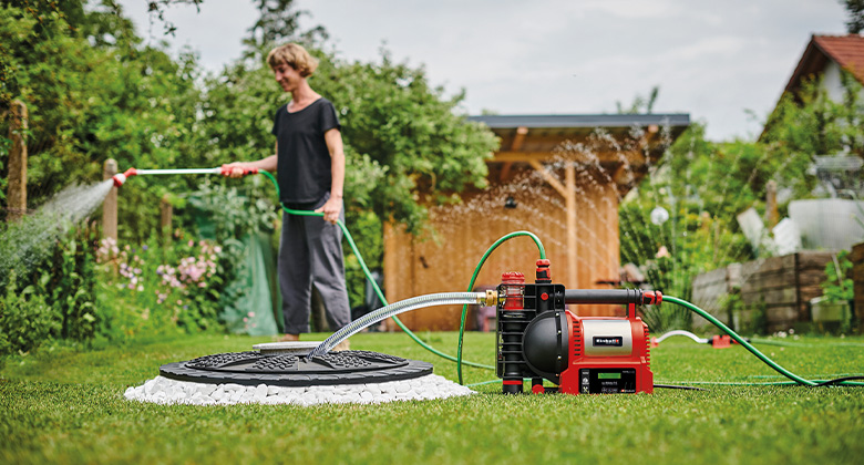 eine Frau bewässert den Rasen mithilfe einer Einhell Gartenpumpe