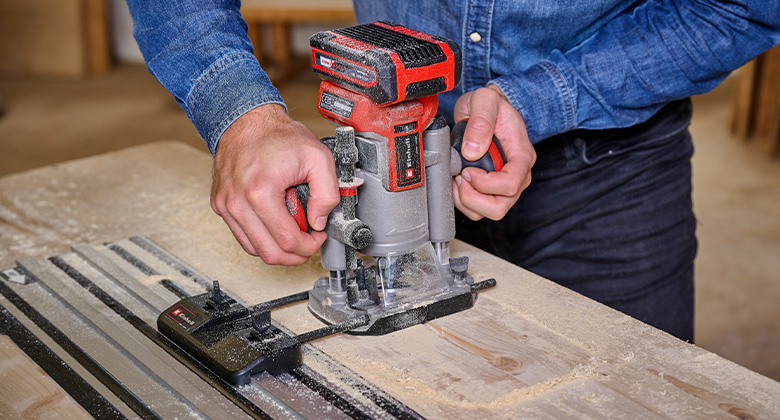 Eine Einhell Akku-Oberfräse wird mit einer Führungsschiene verwendet, um präzise in Holz zu fräsen.