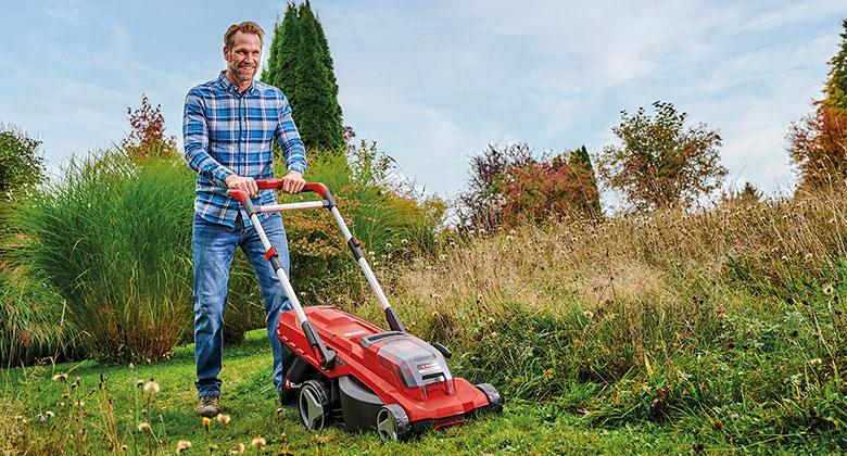 Ein Mann mäht hohes Gras mit einem Akku-Rasenmäher.