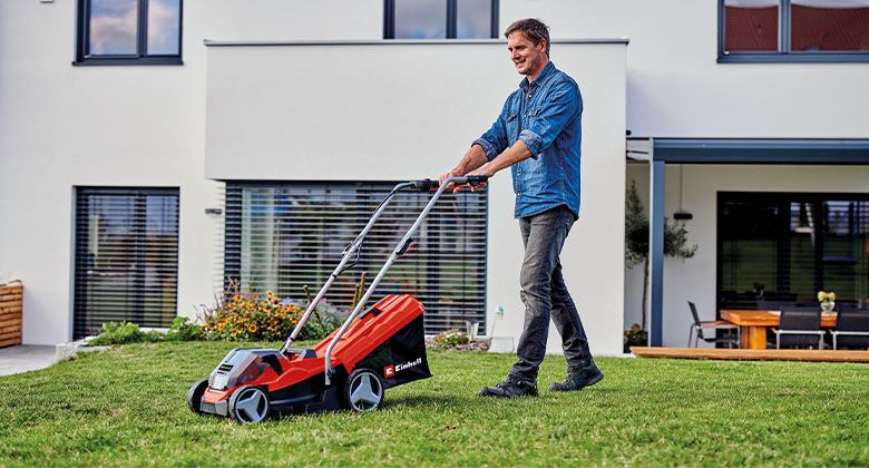 Ein Mann mäht eine kleine Rasenfläche vor seinem Haus mit einem Akku-Rasenmäher.