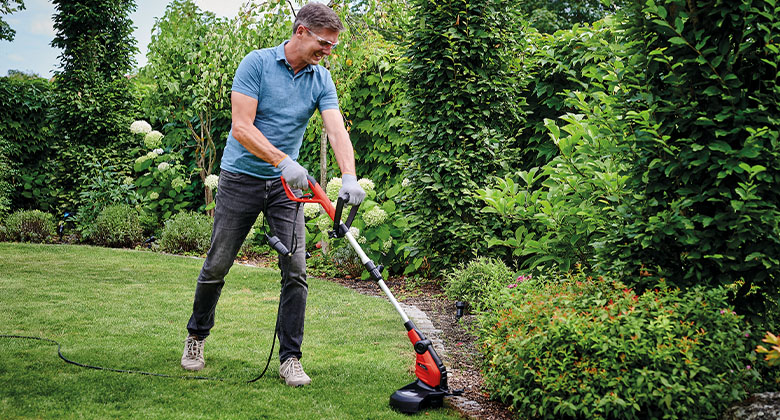 Mann nutzt kabelgebundenen Eletro-Trimmer in einem Garten