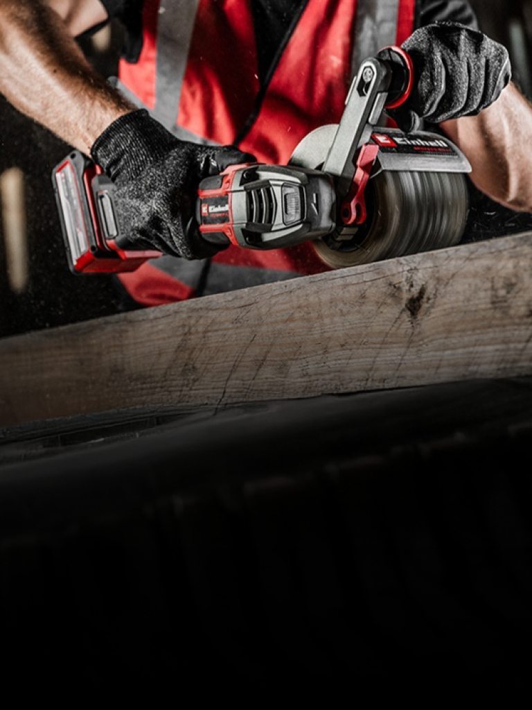 The image shows a person using a red and black Einhell power tool to sand a wooden surface.