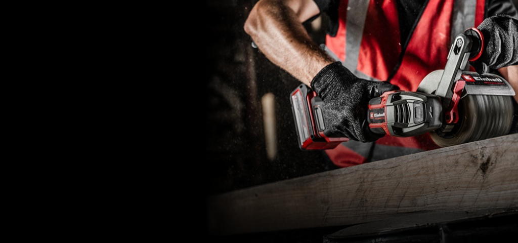 The image shows a person using a red and black Einhell power tool to sand a wooden surface.