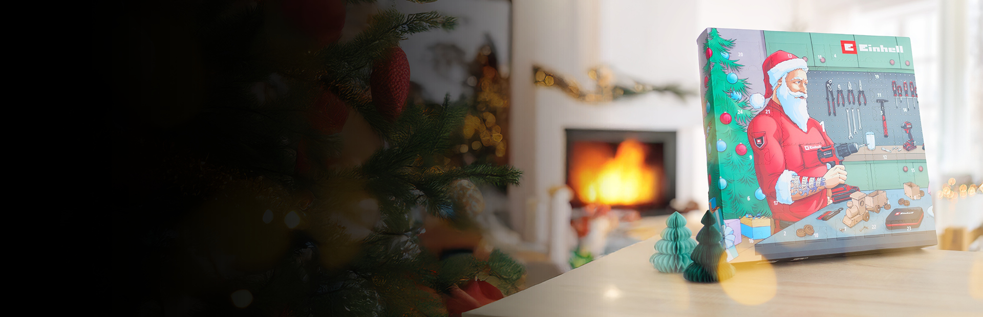 Das Bild zeigt eine gemütliche Weihnachtsszene mit einem geschmückten Baum, einem Kamin und einem Einhell-Adventskalender, auf dem der Weihnachtsmann in einer Werkstatt mit einer Bohrmaschine zu sehen ist.