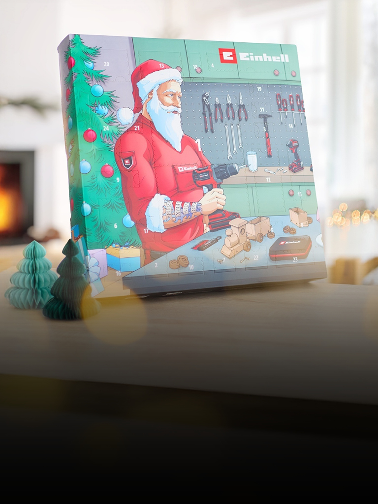 Das Bild zeigt eine gemütliche Weihnachtsszene mit einem geschmückten Baum, einem Kamin und einem Einhell-Adventskalender, auf dem der Weihnachtsmann in einer Werkstatt mit einer Bohrmaschine zu sehen ist.