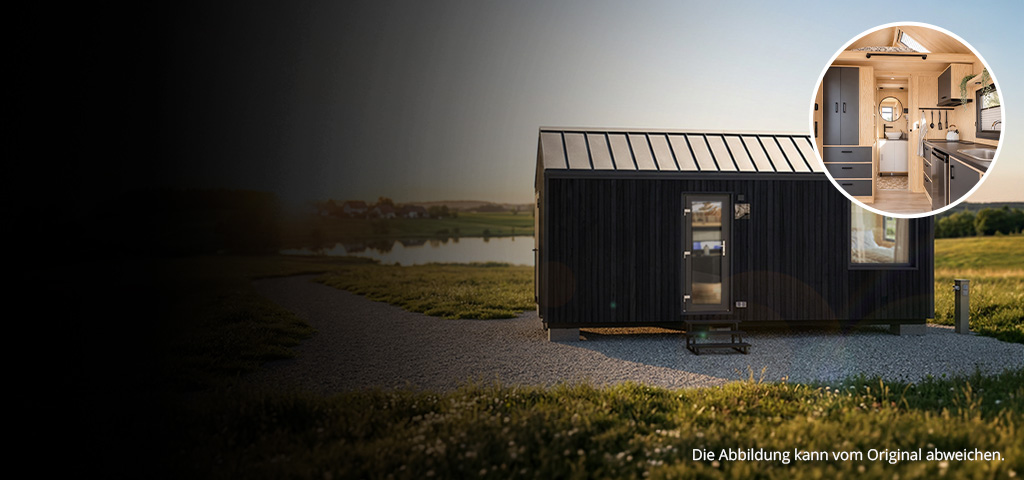 Das Bild zeigt ein modernes Tiny House mit schwarzer Außenfassade auf einem Kiesplatz in einer ländlichen Landschaft nahe einem Gewässer, umgeben von Grünflächen. Eine kreisförmige Einblendung zeigt das Innere mit einer kompakten Küche und einem kleinen Badezimmer in heller Holzoptik.