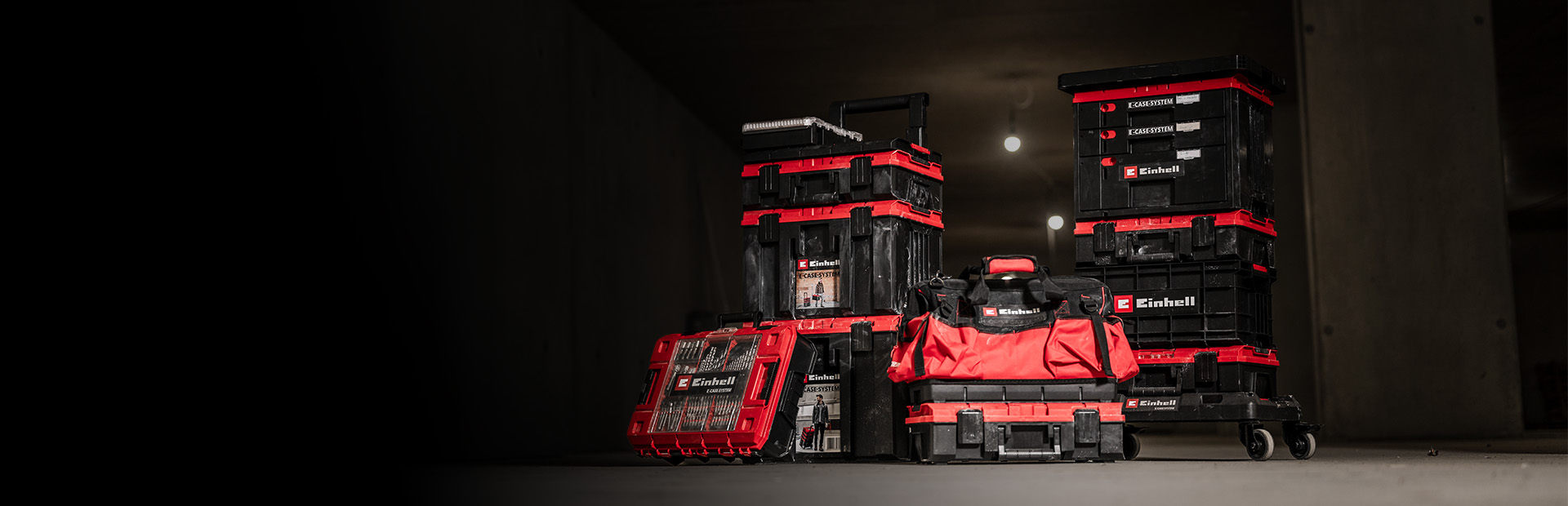 The banner shows a set of stacked Einhell E-Cases and a red-and-black tool bag arranged on a wheeled cart. They are placed in a dim, industrial-looking environment with focused lighting that highlights the products.