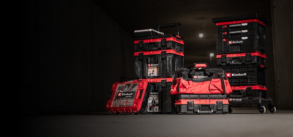The banner shows a set of stacked Einhell E-Cases and a red-and-black tool bag arranged on a wheeled cart. They are placed in a dim, industrial-looking environment with focused lighting that highlights the products.