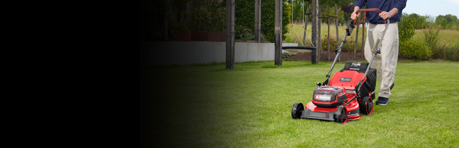 Eine Person mäht einen grünen Rasen mit einem roten Rasenmäher in einem angelegten Garten. Im Hintergrund sind Bäume, Pflanzen und moderne Gartenelemente zu sehen.
