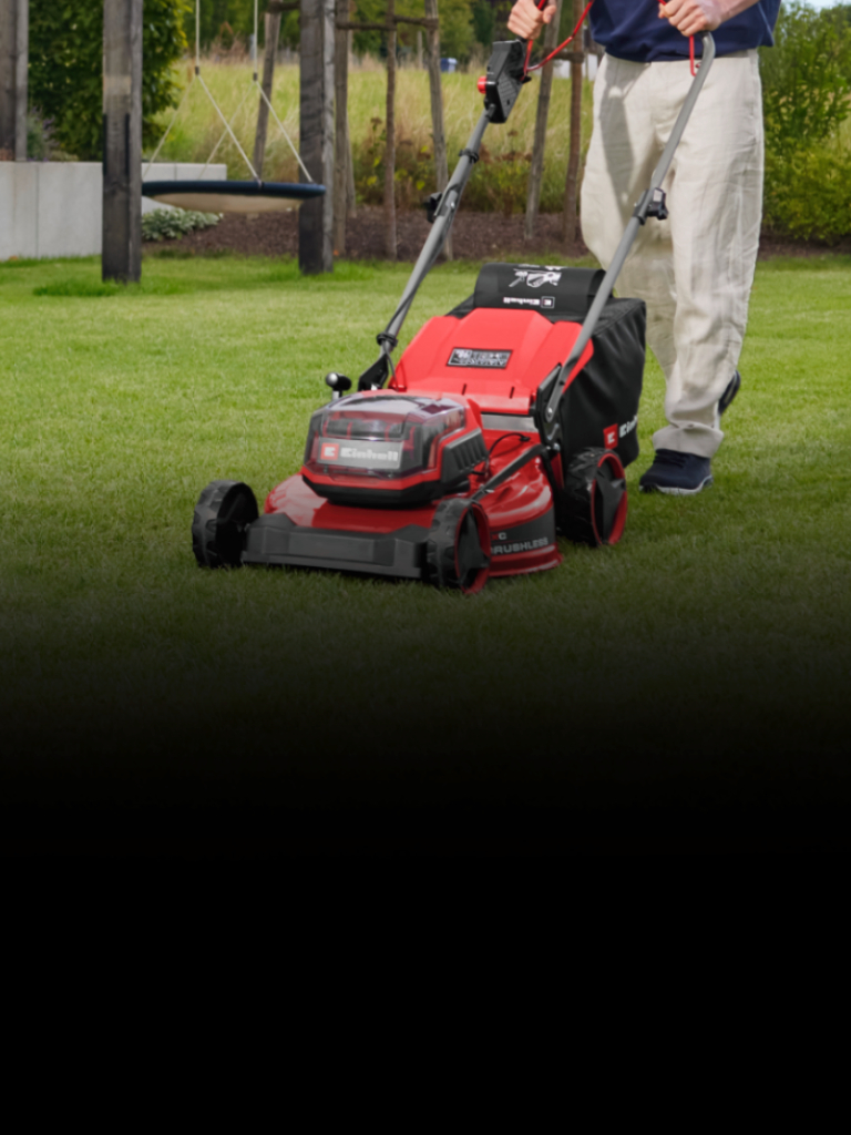 Eine Person mäht einen grünen Rasen mit einem roten Rasenmäher in einem angelegten Garten. Im Hintergrund sind Bäume, Pflanzen und moderne Gartenelemente zu sehen.