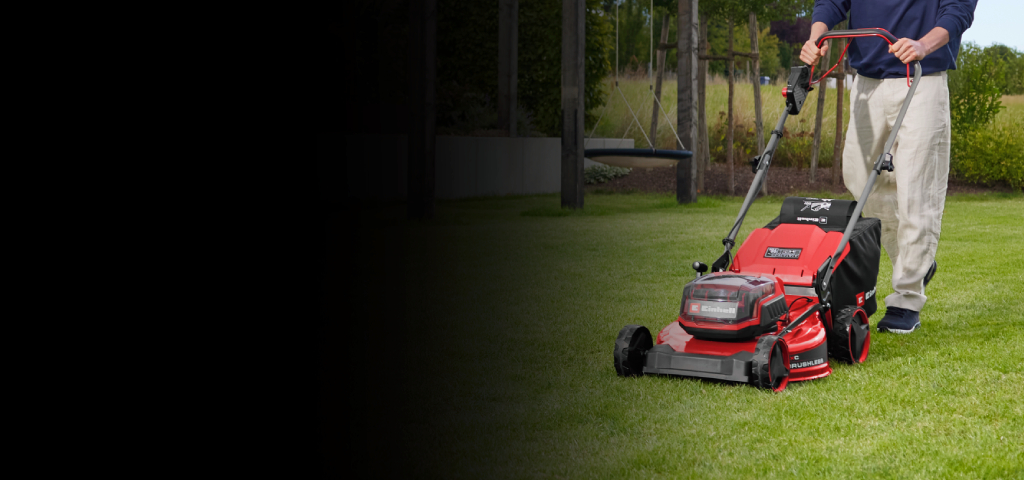 Eine Person mäht einen grünen Rasen mit einem roten Rasenmäher in einem angelegten Garten. Im Hintergrund sind Bäume, Pflanzen und moderne Gartenelemente zu sehen.