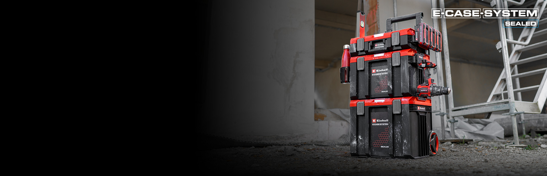 Ein Stapel von Einhell SEALED E‑Cases steht auf einer Baustelle vor einem Gerüst. Die robusten Koffer sind sicher miteinander verbunden und für die mobile Werkzeugaufbewahrung ausgelegt.