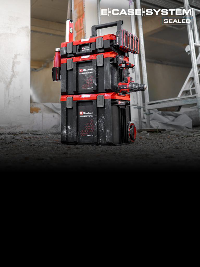 Ein Stapel von Einhell SEALED E‑Cases steht auf einer Baustelle vor einem Gerüst. Die robusten Koffer sind sicher miteinander verbunden und für die mobile Werkzeugaufbewahrung ausgelegt.