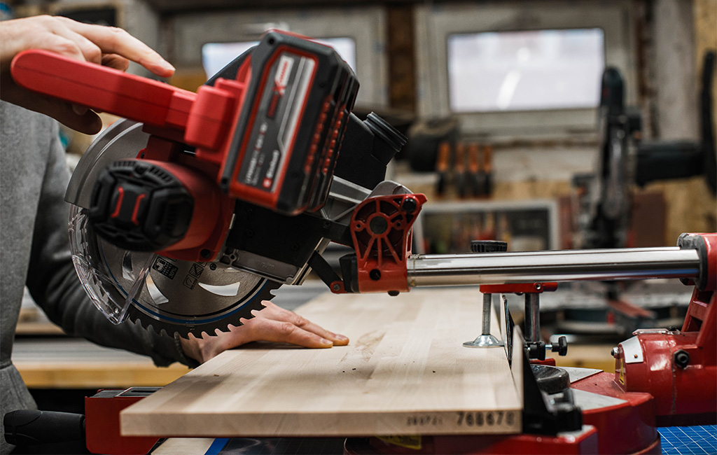 Eine Person arbeitet mit einer Einhell Akku-Kappsäge an einem hellen Holzbrett in der Werkstatt.