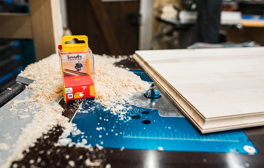 Holzfräser auf Werkbank mit Holzspänen und gefrästem Holzbrett.