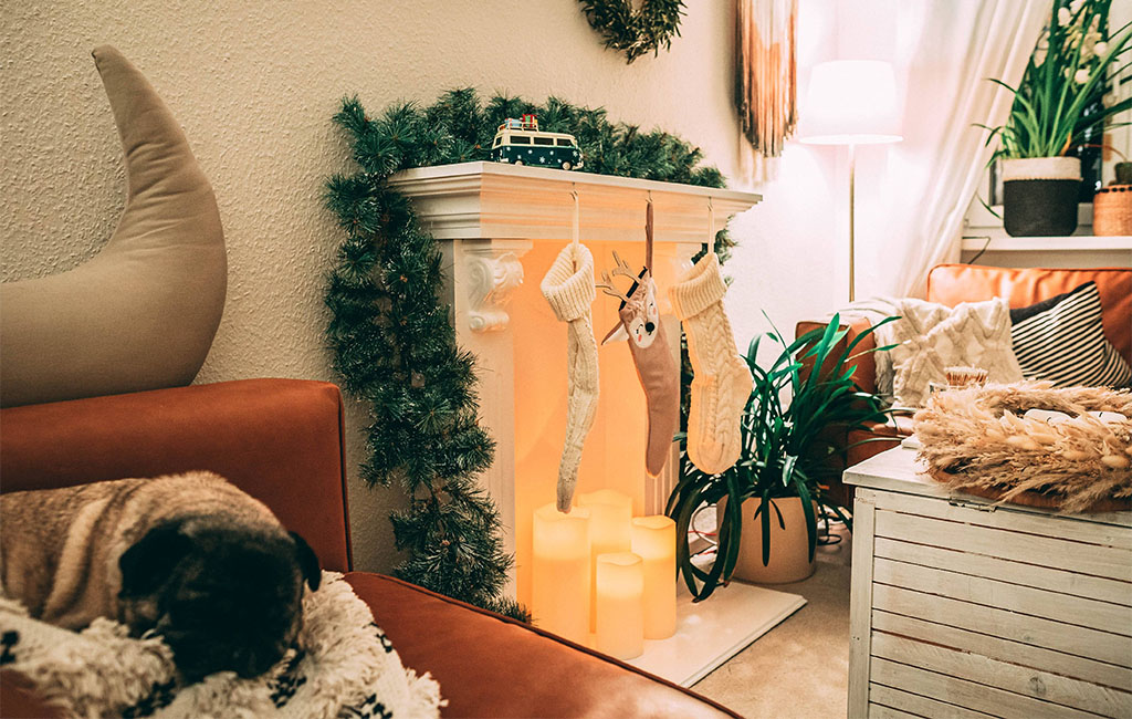 Weihnachtlich geschmücktes Wohnzimmer mit Kaminattrappe, LED-Kerzen, Strümpfen und einem schlafenden Mops auf dem Sofa.