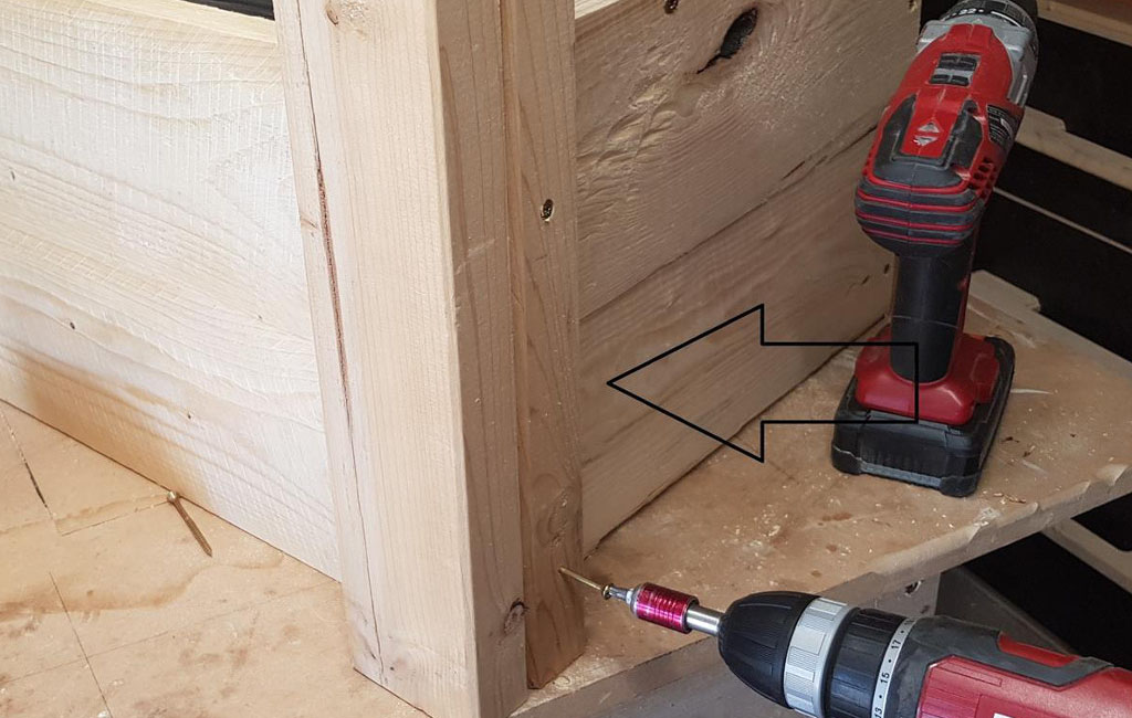 Ein Holzbein wird mit einem Einhell Akkuschrauber an die Seite eines Holzkastens geschraubt, ein Pfeil zeigt auf die Stelle.